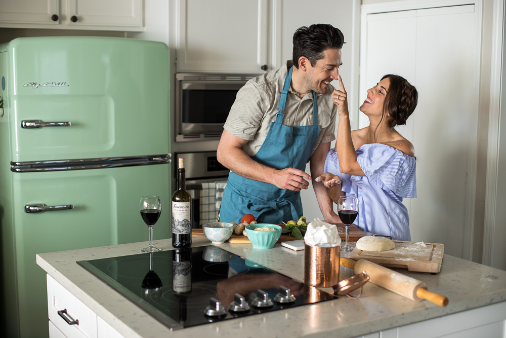 Lifestyle blogger Devin McGovern and wife Marlene Martinez in the kitchen with pizza and wine